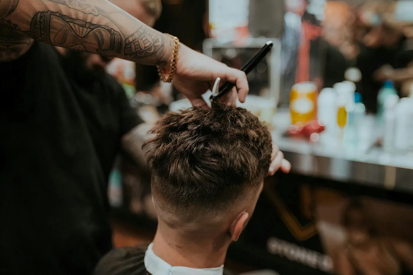A barber using scissors and a comb to cut the top of a client’s hair in a busy barbershop.