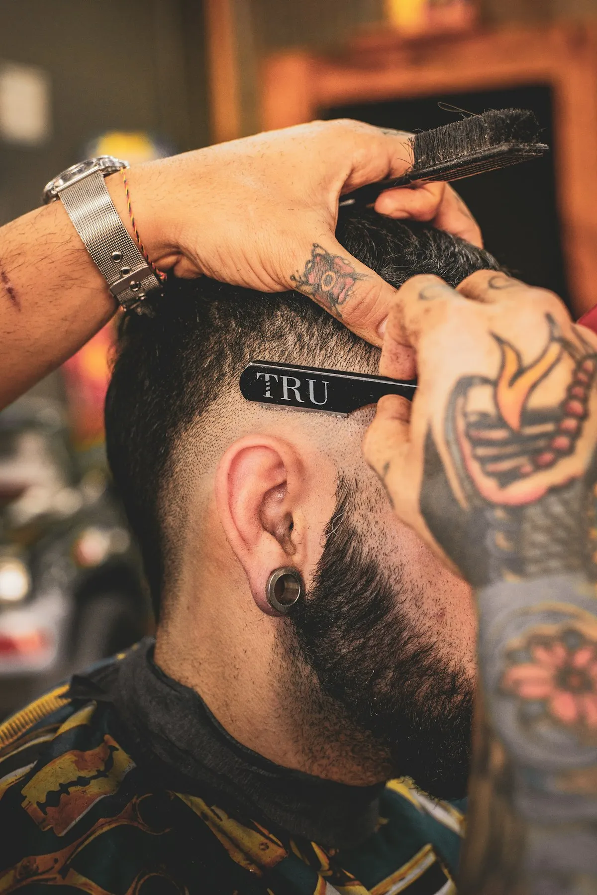 Close-up of a barber using clippers and a straight razor to line up a skin fade on a client’s head.