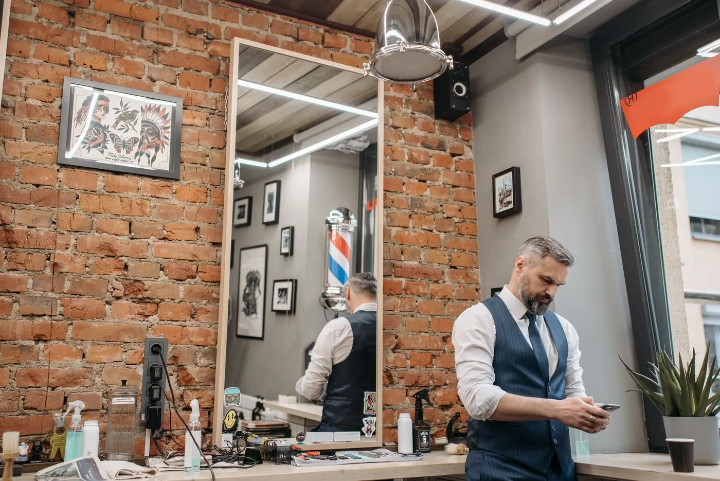 A barber standing in his shop looking down at a booking confirmation on his mobile phone.
