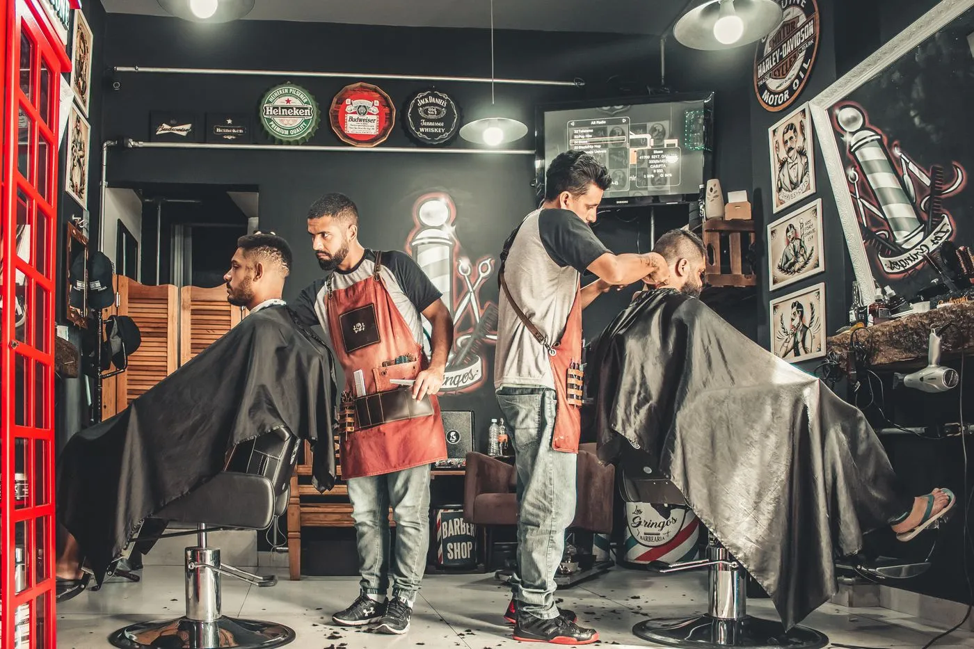 A busy barbershop floor with two barbers cutting hair for two clients at neighbouring chairs.